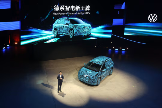 一名男子在台上展示经过伪装的大众 ID.AURA T6 纯电动汽车。